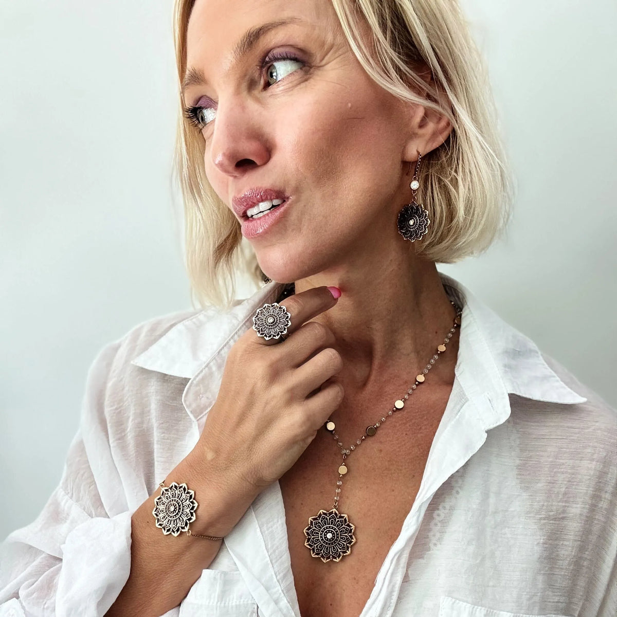Woman wearing jewelry including a necklace, bracelet, and ring against a plain background
