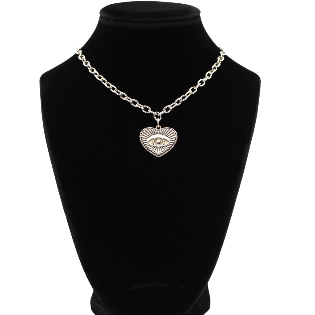 silver chain choker with a heart-shaped eye pendant, bar clasp, and crescent moon charm. Its mixed metal design adds a unique flair, all set against a white background.