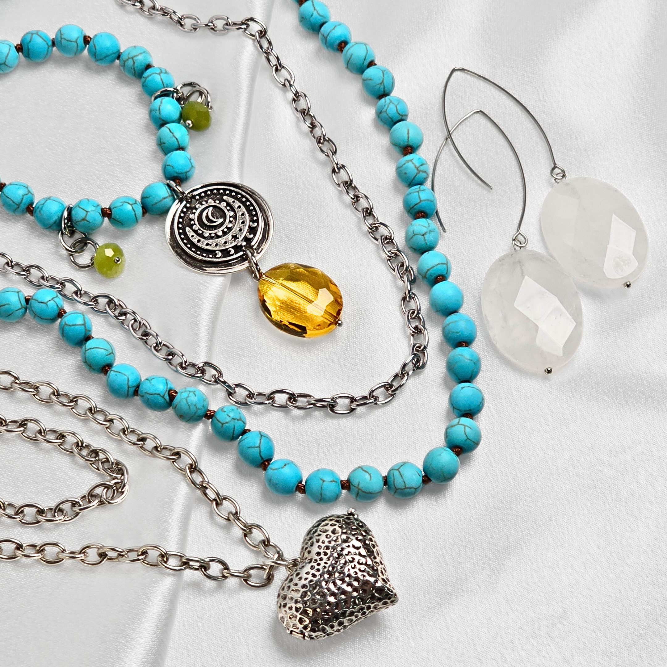 Turquoise beaded necklace with a heart pendant and clear earrings on a white background