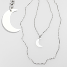 Two silver moon-shaped pendants on chains against a light gray background