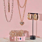 Jewelry set including necklaces, bracelets, and hoop earrings on a pink background