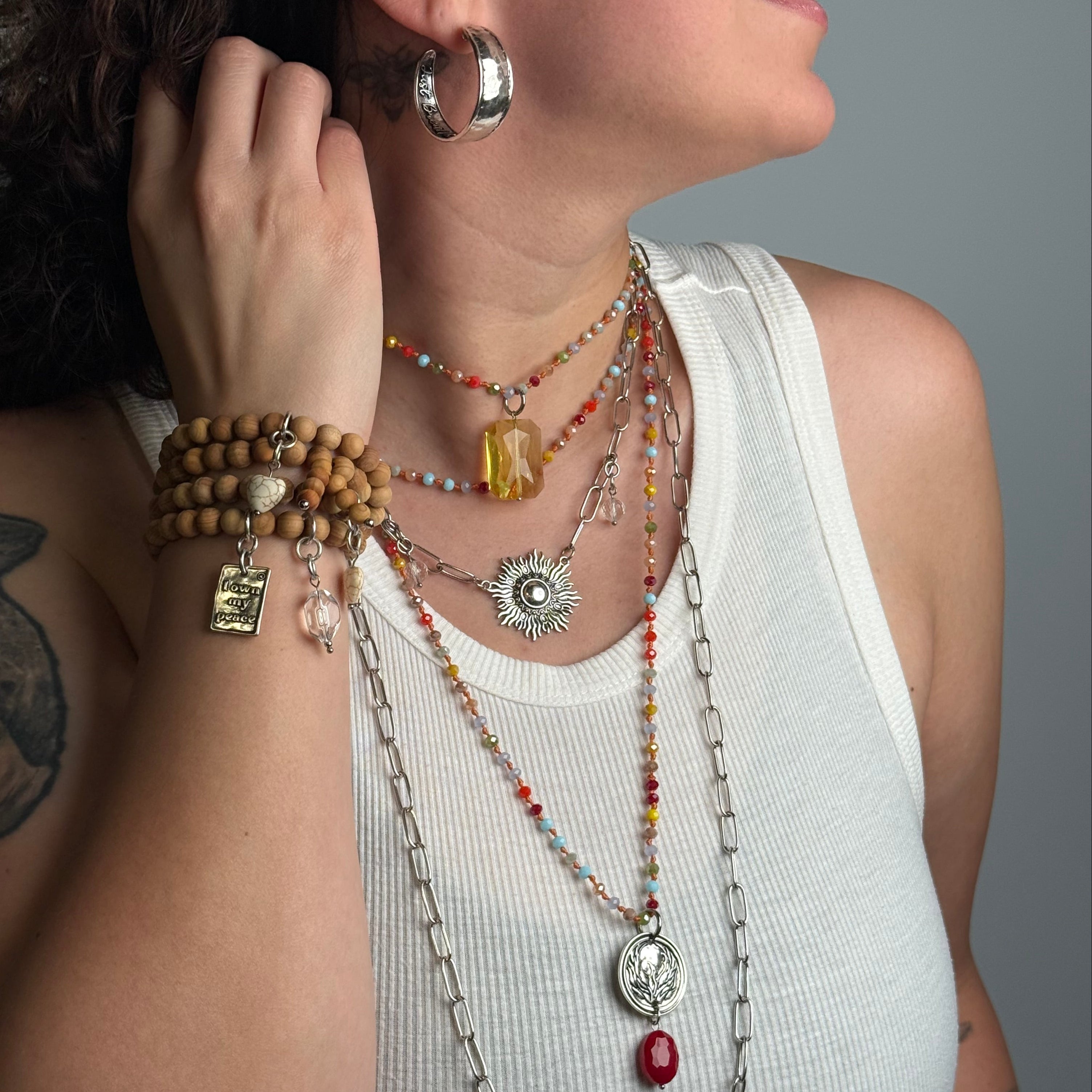 Woman wearing multiple necklaces, bracelets, and earrings with a neutral background