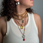 Person wearing a white tank top with multiple necklaces and a ring on a neutral background