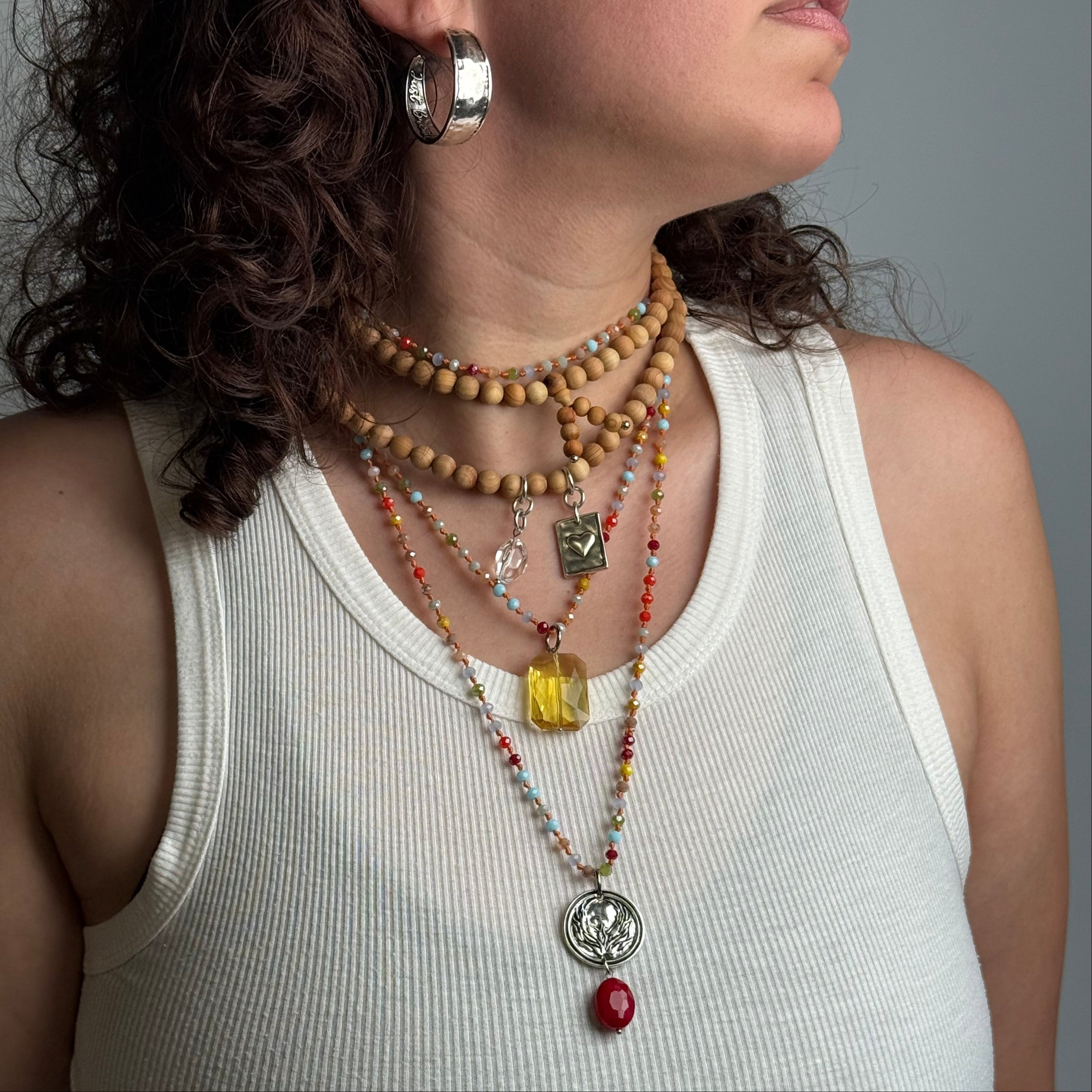 Person wearing a white tank top with multiple necklaces and a ring on a neutral background