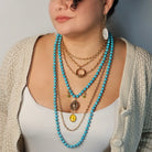 Person wearing multiple necklaces with turquoise beads and gold chains.