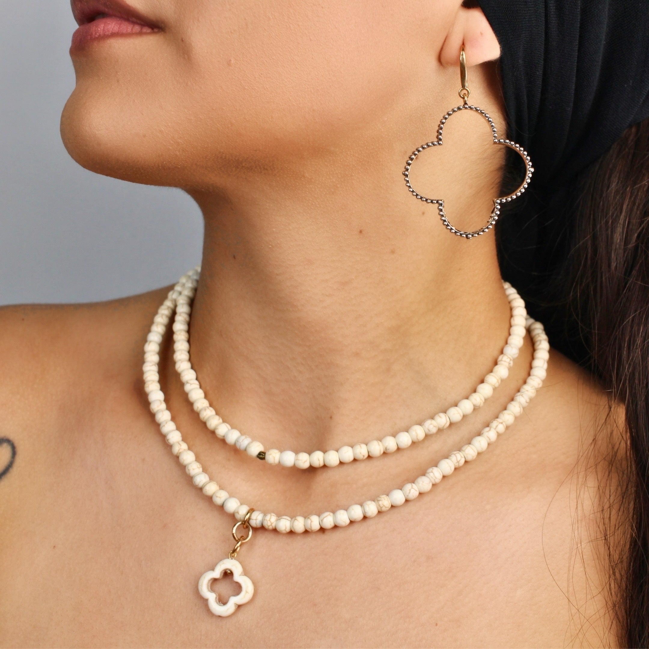 Close-up of a woman wearing a pearl necklace and hoop earrings against a neutral background